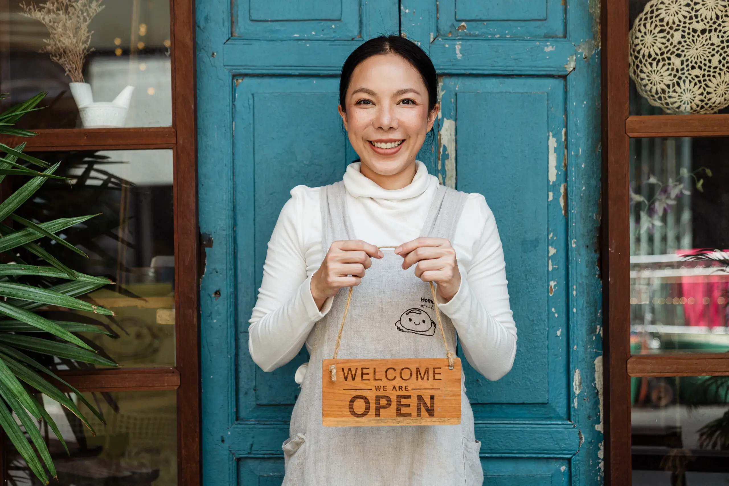 Ethnic female cafe owner showing welcome we are open inscription